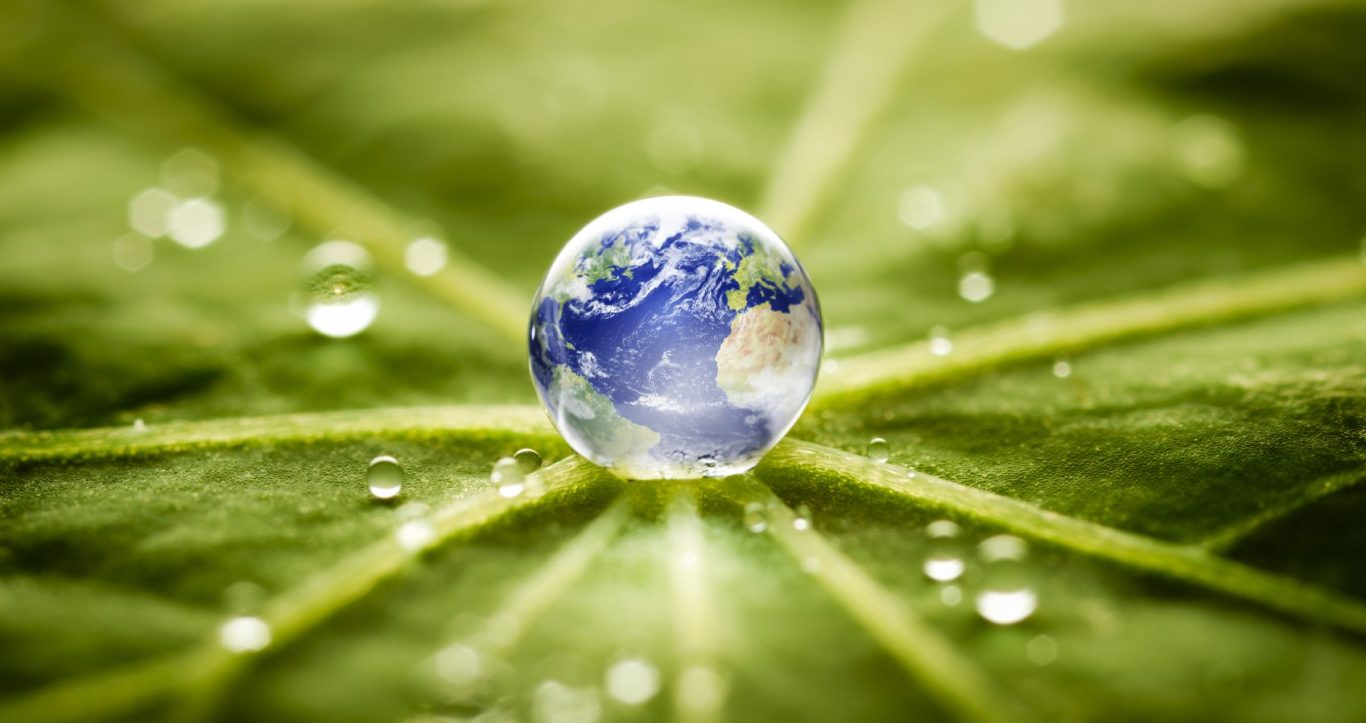 Ein Wassertropfen in form der Erde auf einem grünen Blatt